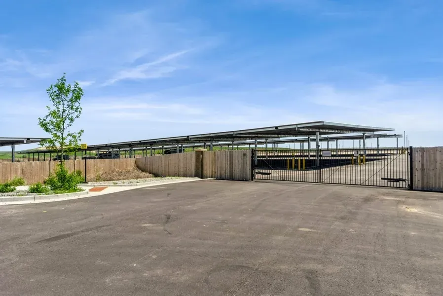 An access gate and wooden fence protect a lot of covered parking spaces.