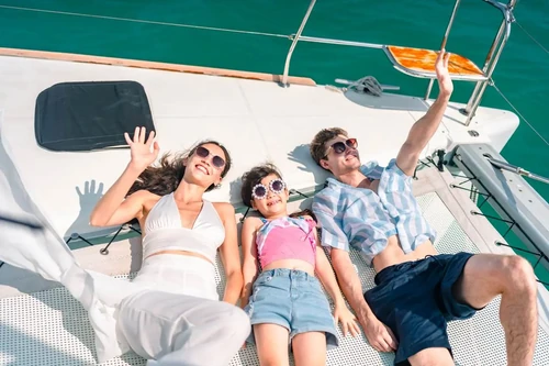A family relaxing and waving on a boat deck under the sun, enjoying a summer day out on the water.