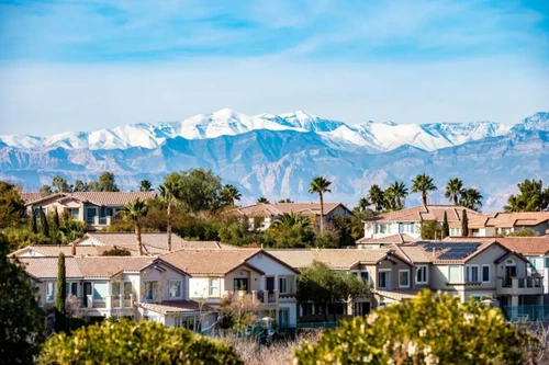 A suburban Las Vegas neighborhood with palm trees and snowcapped mountains on a clear day.