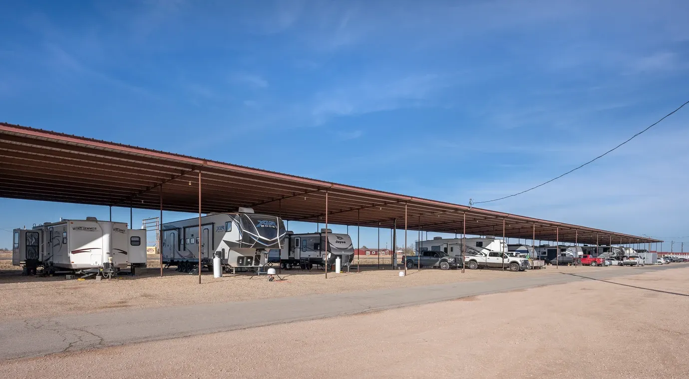 RVs stored under a tan roof during a sunny day with blue skies.