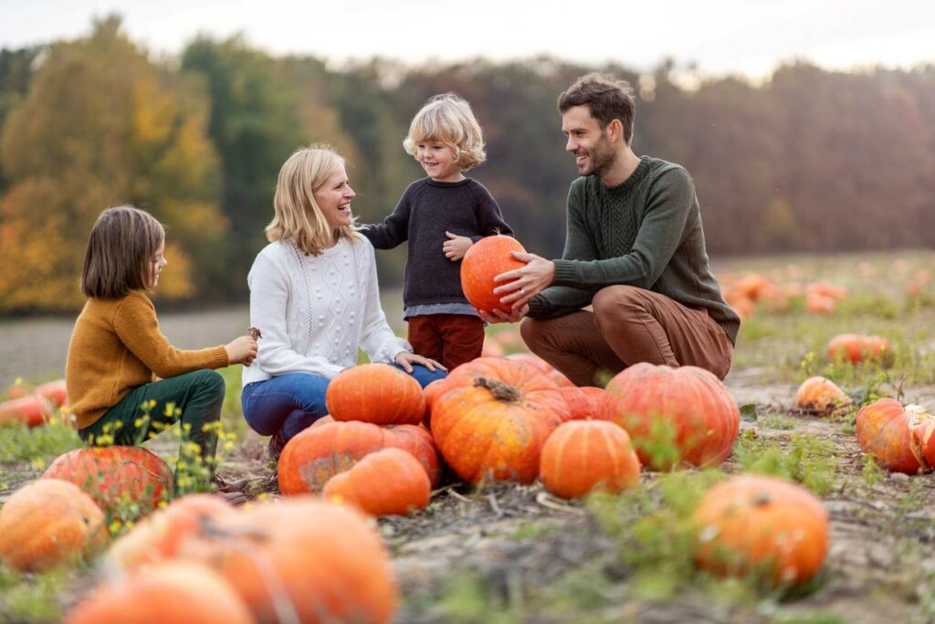 Happy young family in a pumpkin patch field in the fall.