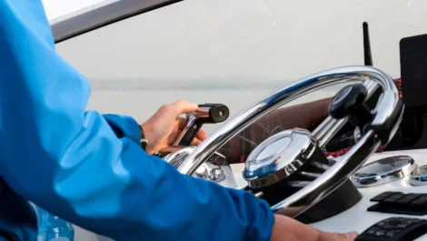 A close-up of a man’s hands on the steering wheel of a motor boat.