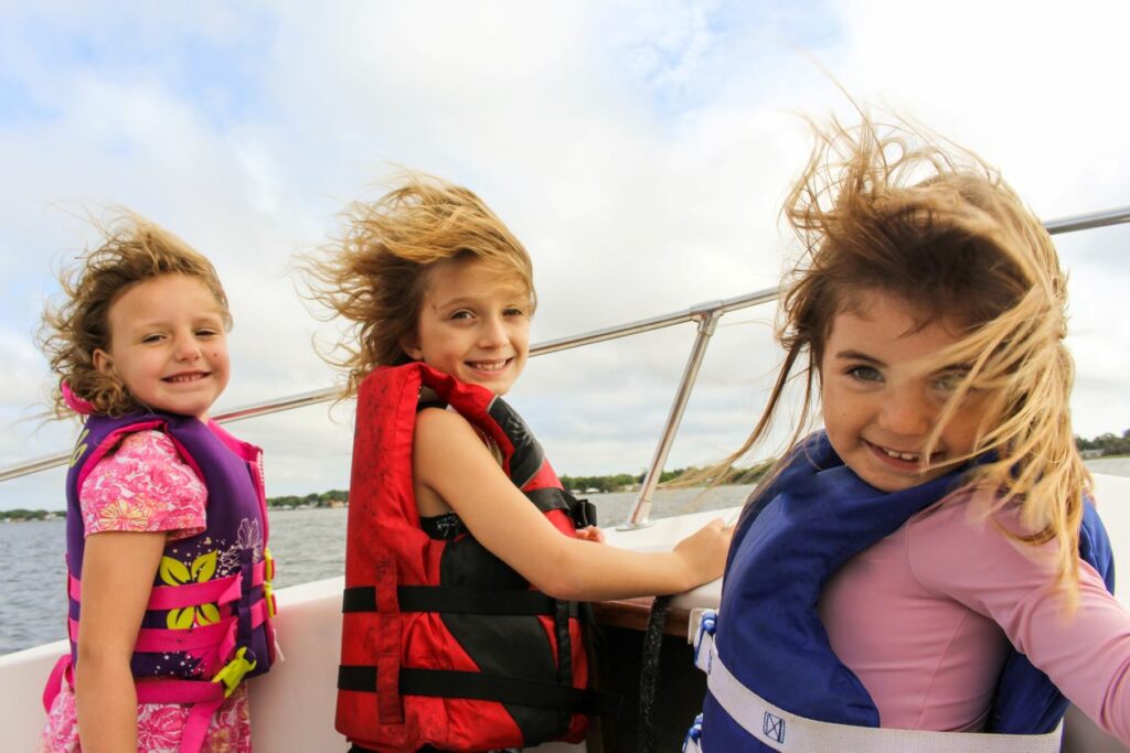 Three kids smiling and wearing life jackets on a boat. 