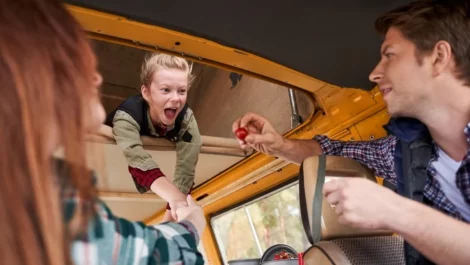 A young blonde girl in an RV is delighted to be given a cherry tomato by her father.