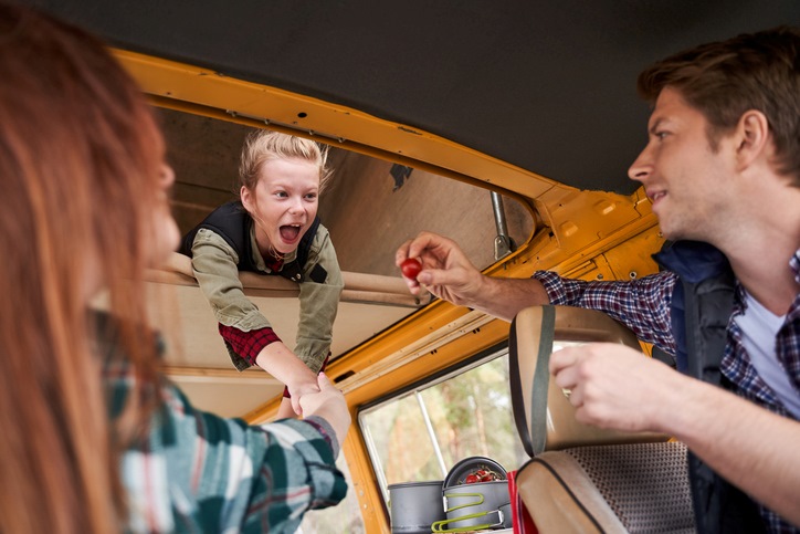 A young blonde girl in an RV is delighted to be given a cherry tomato by her father.