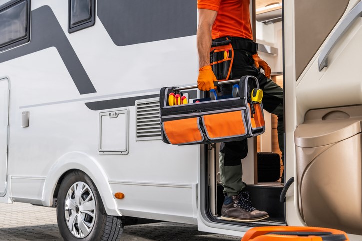 A man entering an RV with a stocked toolkit to conduct mechanical checks.