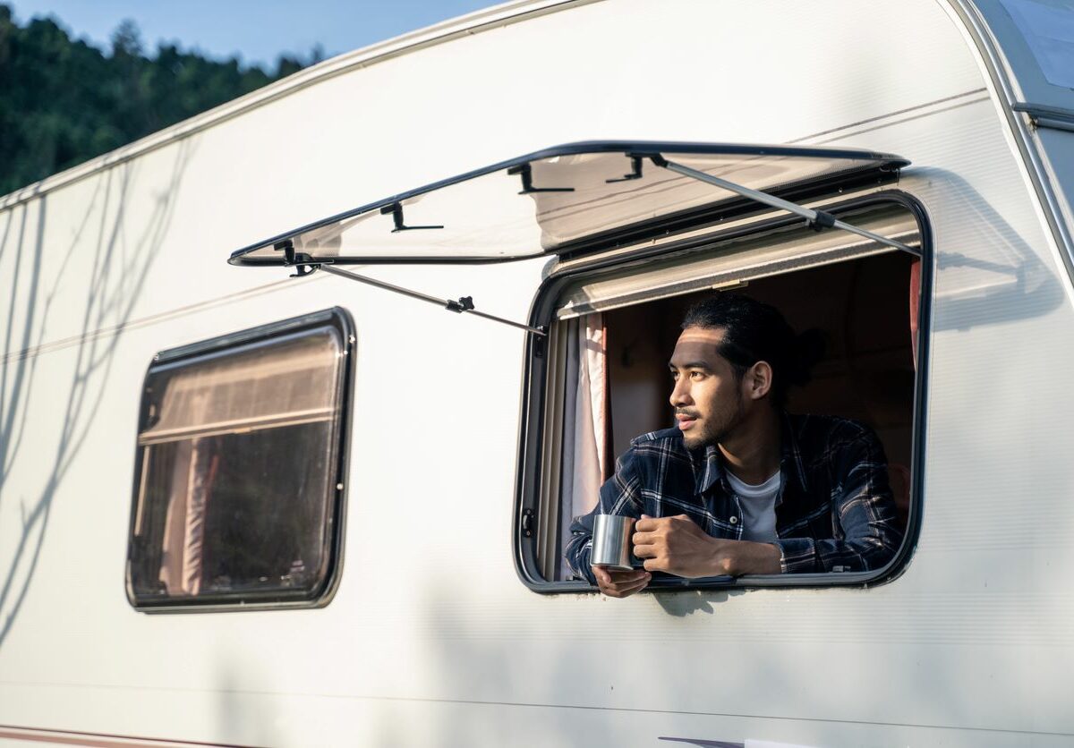 A young man drinking coffee while looking out his RV window.