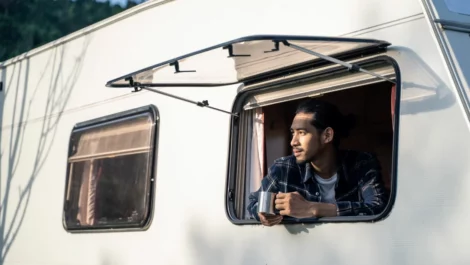 A young man drinking coffee while looking out his RV window.