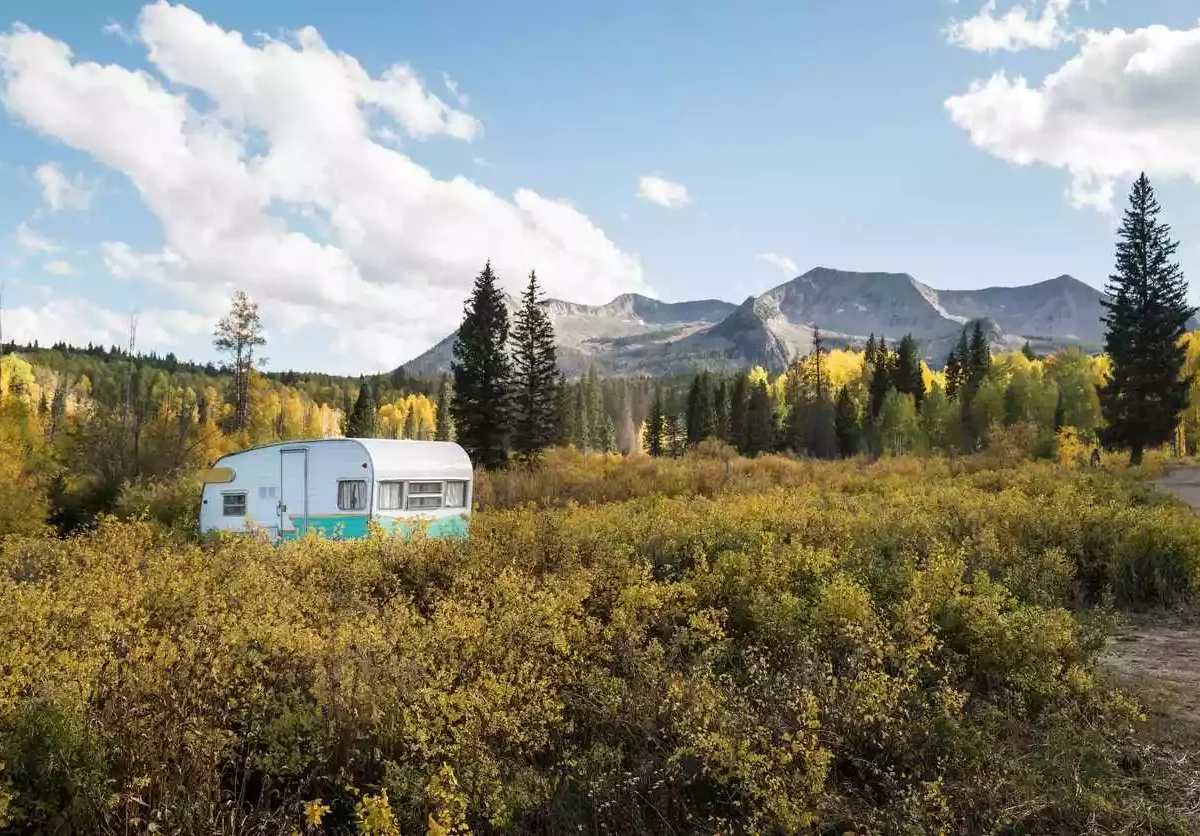 A camper parked amid autumn foliage with Colorado mountains looming.