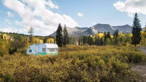 A camper parked amid autumn foliage with Colorado mountains looming.