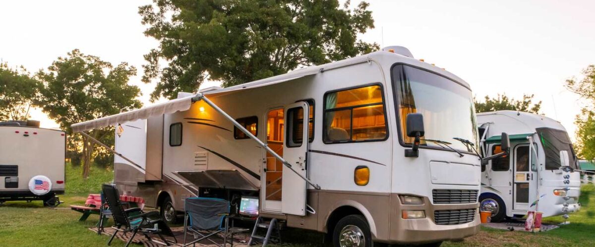 An RV parked in a grassy area with an extended awning, outdoor chairs, and a camping setup.