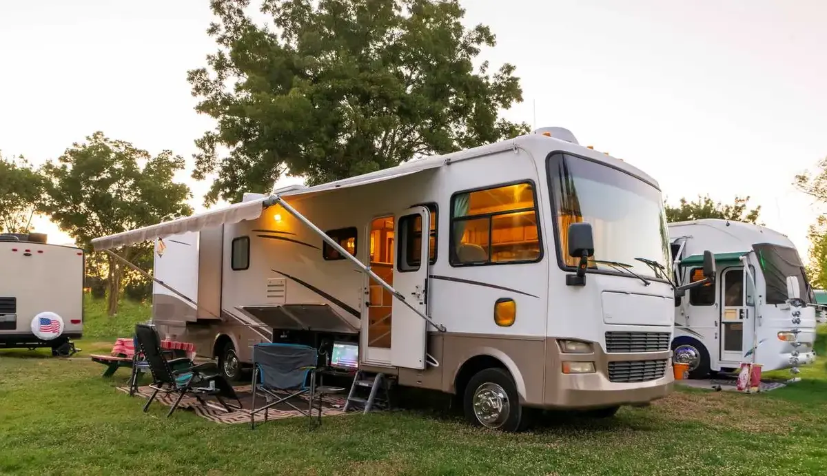 An RV parked in a grassy area with an extended awning, outdoor chairs, and a camping setup.