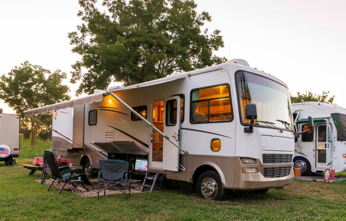 An RV parked in a grassy area with an extended awning, outdoor chairs, and a camping setup.