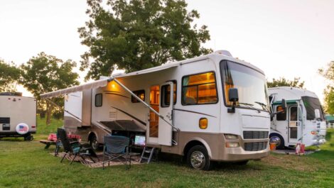 An RV parked in a grassy area with an extended awning, outdoor chairs, and a camping setup.