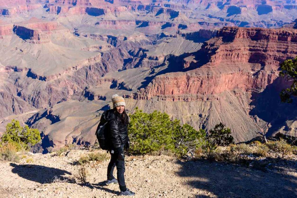 A hiker wearing winter clothing stands at the edge of the Grand Canyon. 