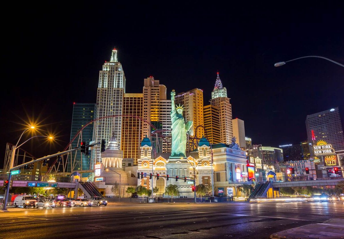 The Las Vegas Strip lit up at night, with buildings in various architectural styles and a smaller scaled version of the Statue of Liberty.