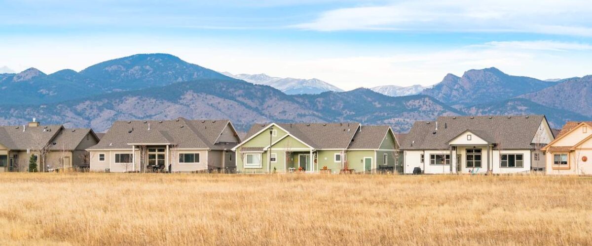 A row of houses in Loveland, CO, with a grass field and scenic Rocky Mountains.