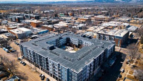 A large modern apartment complex in downtown Loveland, CO, with mountains behind it.