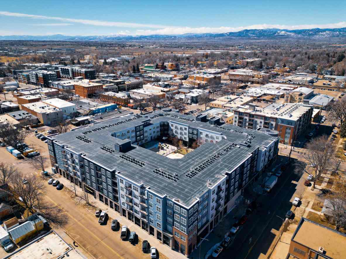 A large modern apartment complex in downtown Loveland, CO, with mountains behind it.