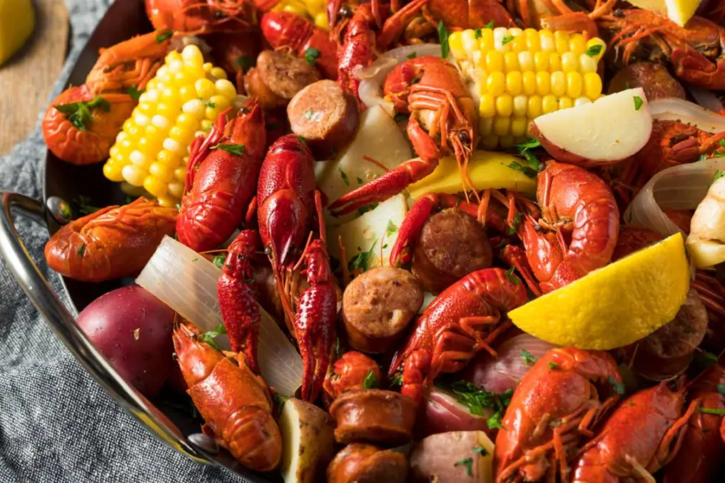 A delicious Cajun-style crawfish boil with corn, sausage, potatoes, onions, and lemon wedges served in a large pan.