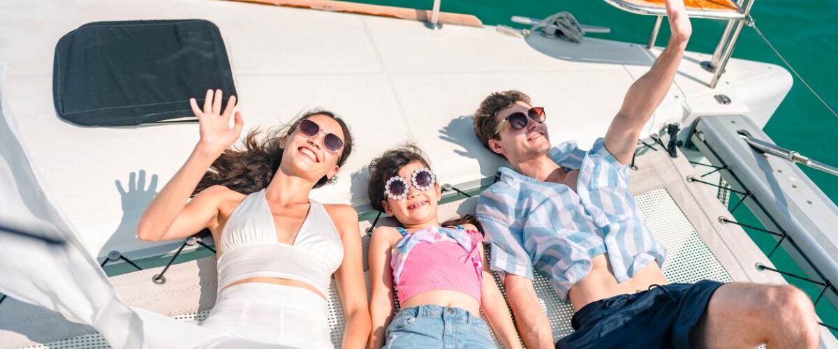 A family relaxing and waving on a boat deck under the sun, enjoying a summer day out on the water.
