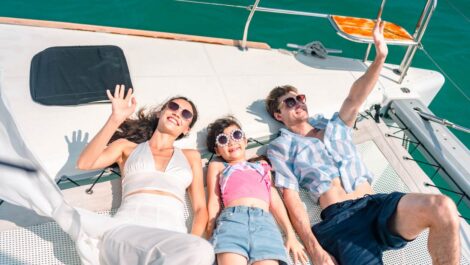 A family relaxing and waving on a boat deck under the sun, enjoying a summer day out on the water.