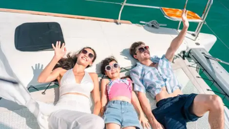 A family relaxing and waving on a boat deck under the sun, enjoying a summer day out on the water.