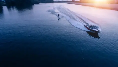 A man water skiing on a lake behind a boat at sunset.