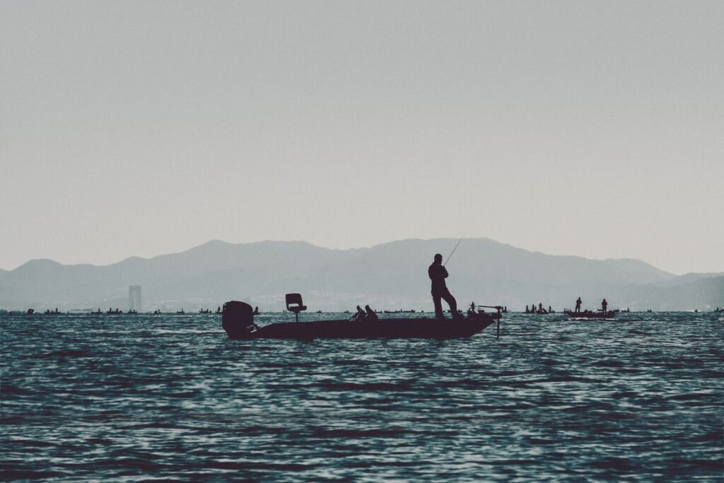 A silhouette of a man fishing on a bass boat on a lake.