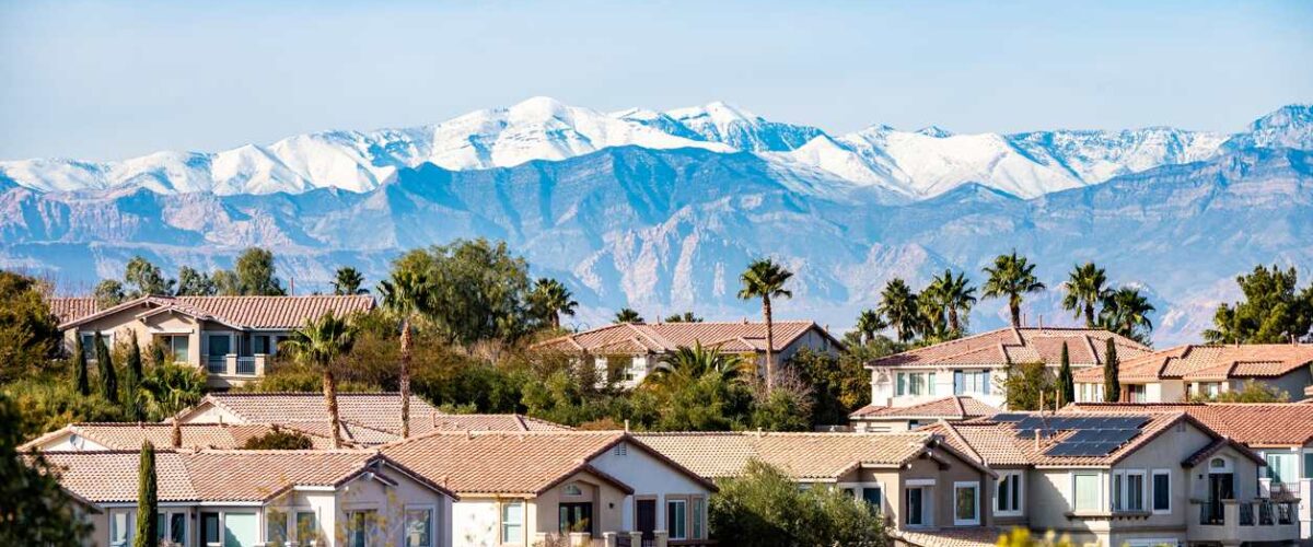 A suburban Las Vegas neighborhood with palm trees and snowcapped mountains on a clear day.