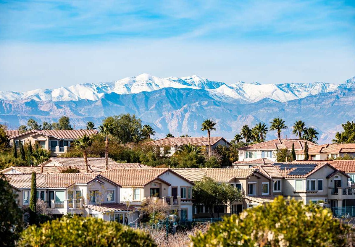 A suburban Las Vegas neighborhood with palm trees and snowcapped mountains on a clear day.
