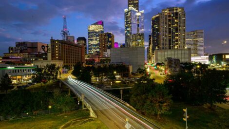 The Downtown Houston skyline at sunset with glowing skyscrapers and a vibrant purple and blue sky.