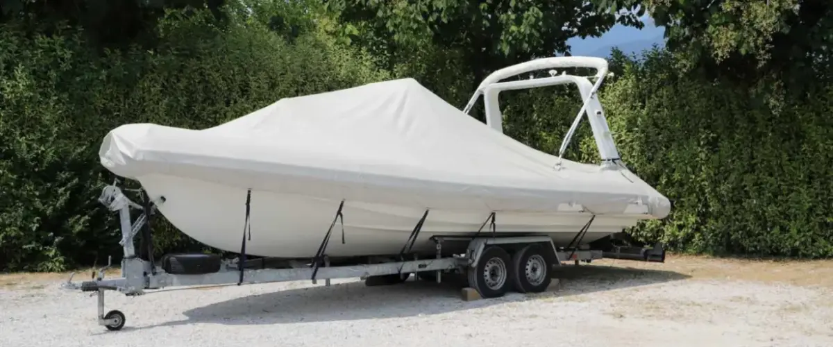 A trailer with a boat on top and covered with a white cover.