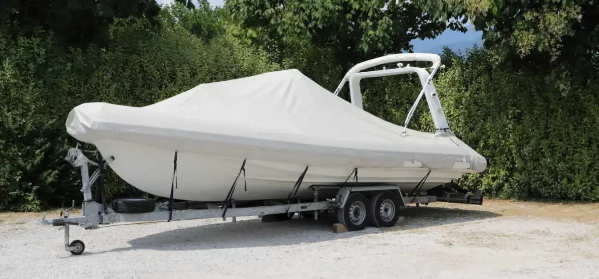 A trailer with a boat on top and covered with a white cover.
