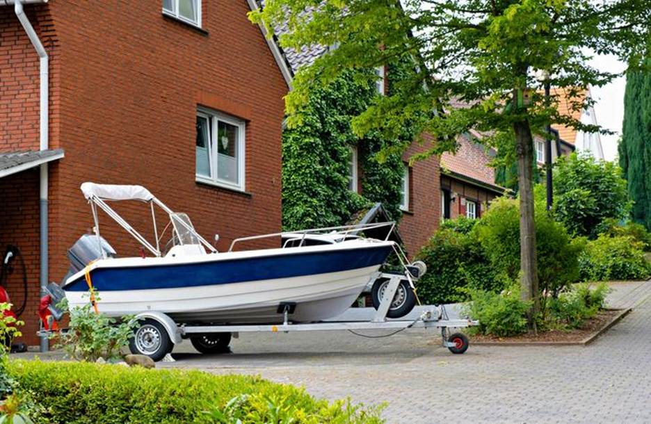 A blue and white boat taking up space on a driveway. 